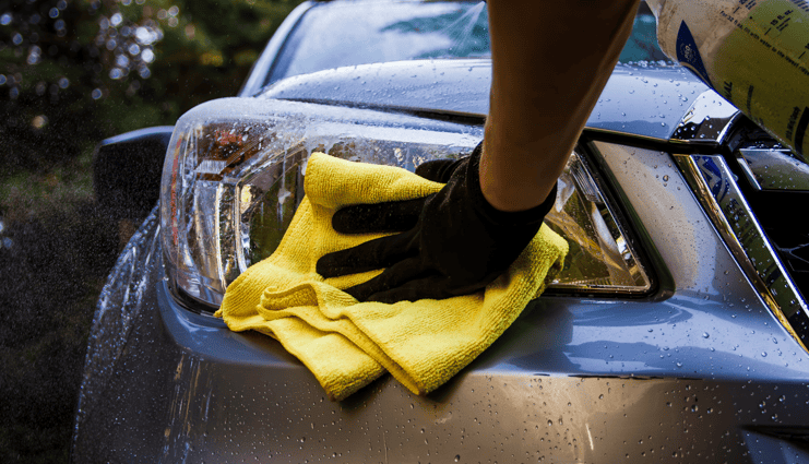 detailer with black gloves wiping headlights on a car parked outside