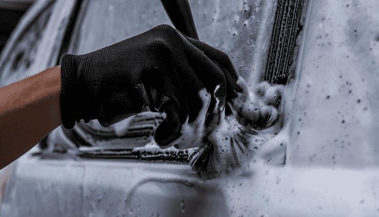 detailer using a brush to scrub seals on the exterior of a car