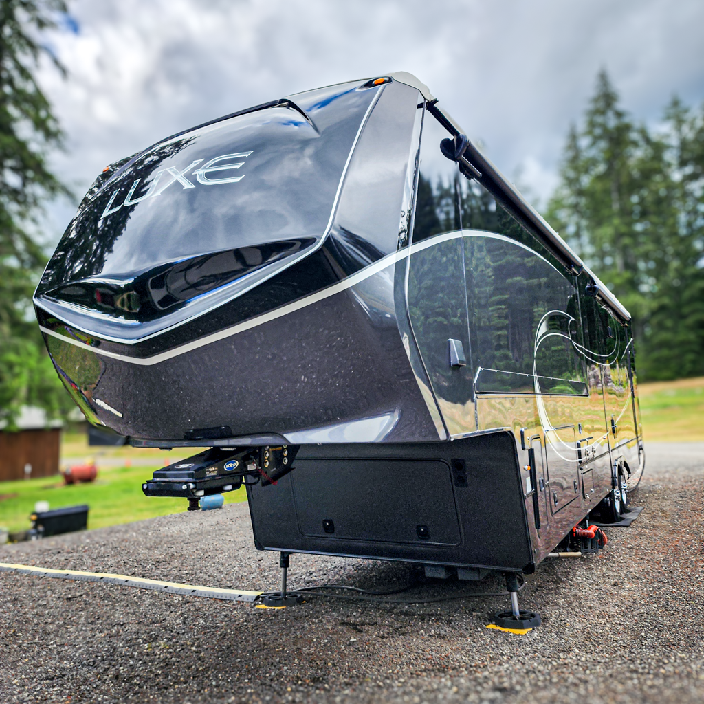 the front and side of a detailed luxe black rv parked on a driveway on a sunny day