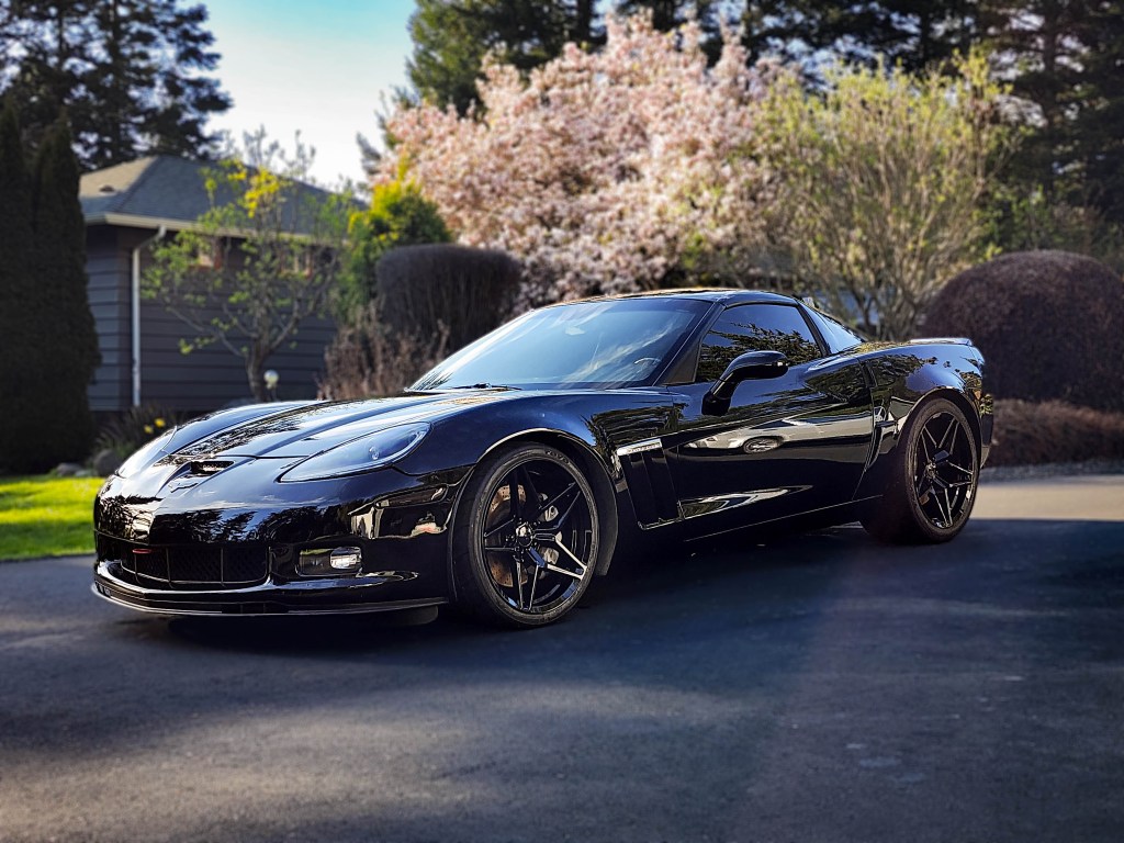 a black grand sport corvette sports car parked in a driveway with trees and house in the background